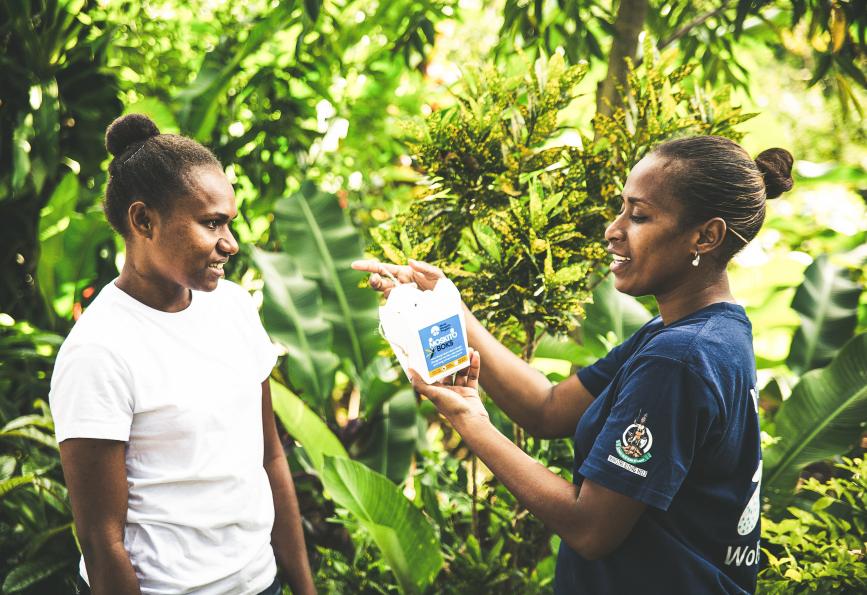 Un membre du personnel de World Mosquito Program au Vanuatu montre à un habitant comment suspendre sa boîte à moustiques.